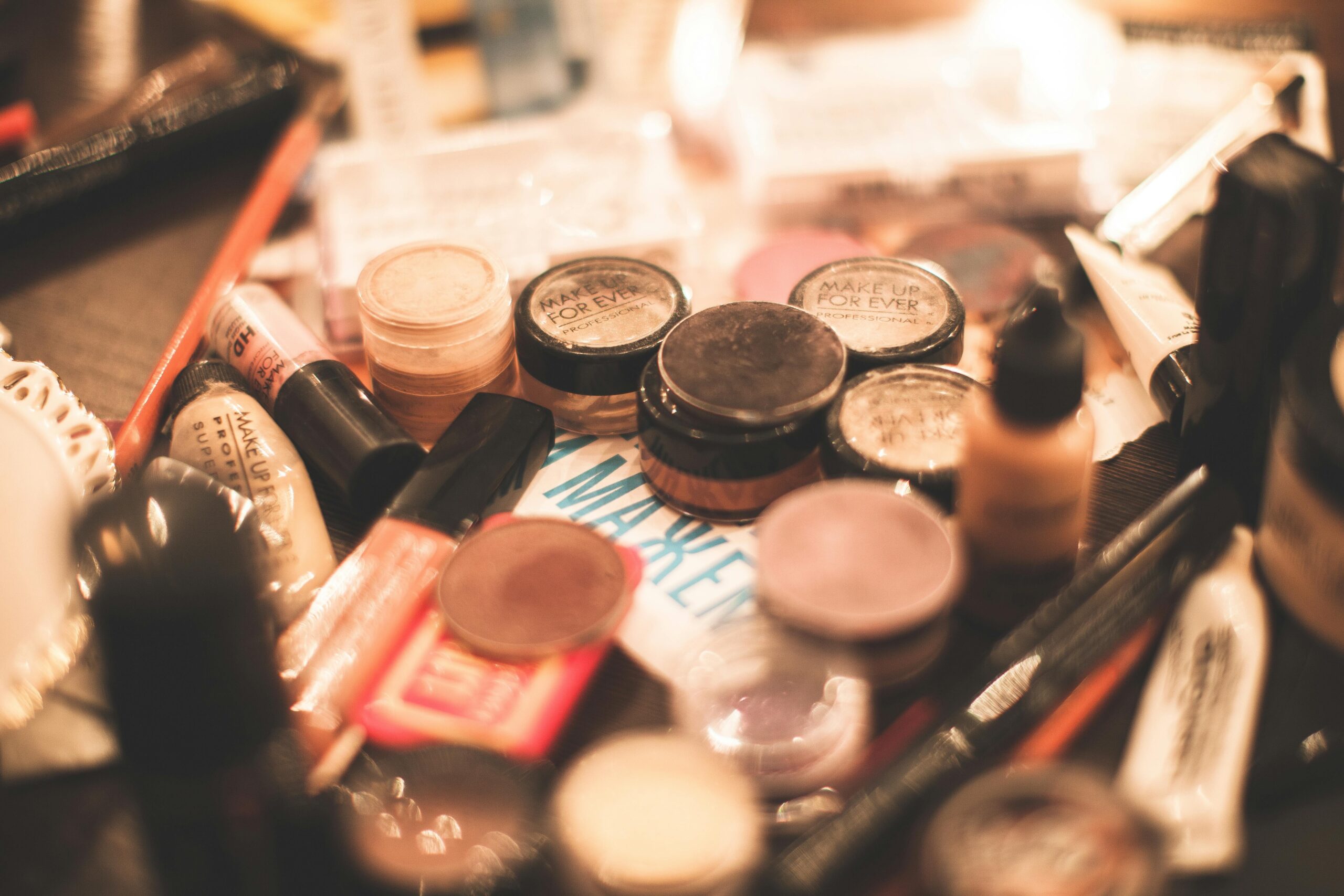 A flat lay photo of essential drugstore makeup products including foundation, mascara, blush, lipstick, and brow pencil